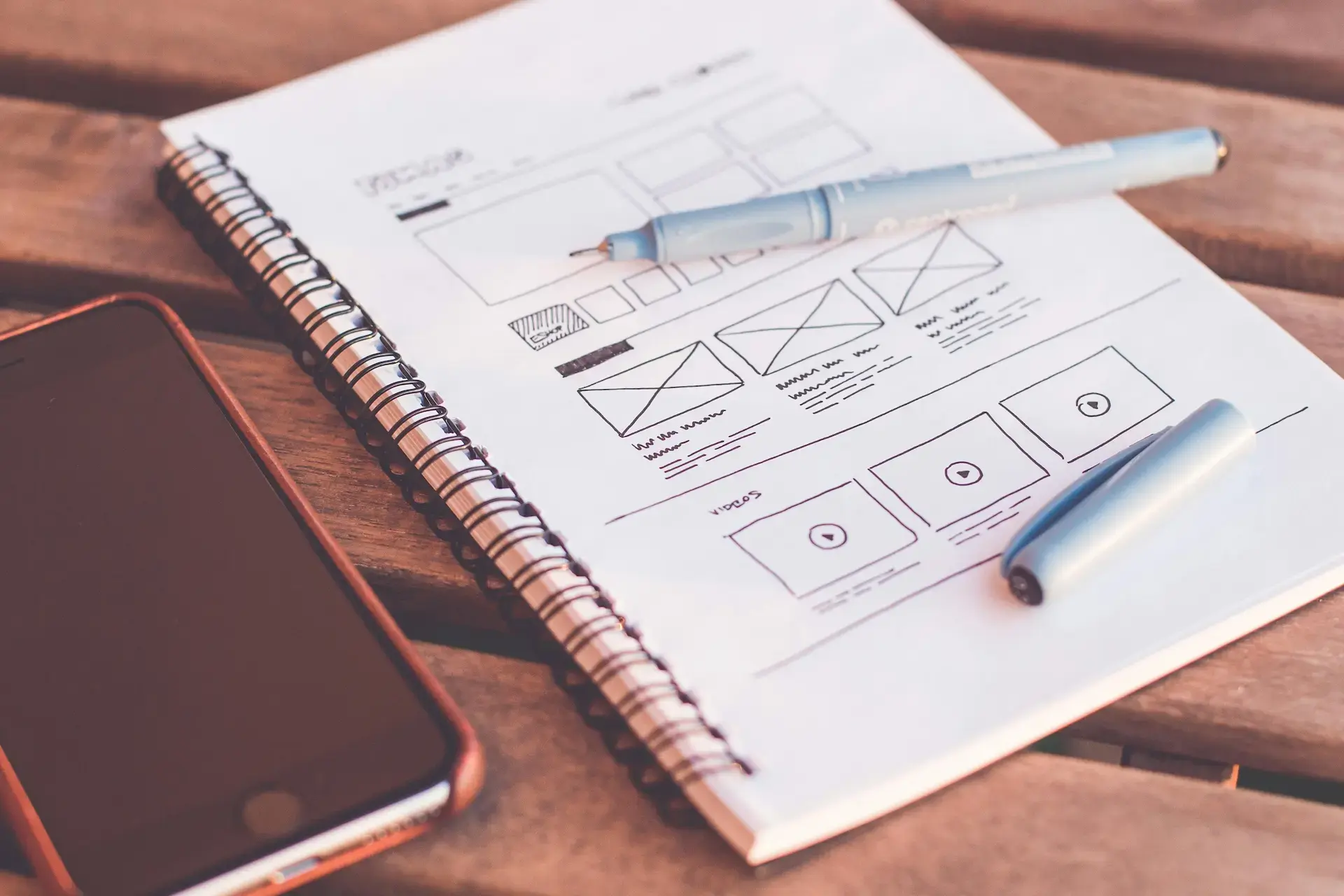 Website wireframe sketch on a notebook with a pen and phone, detailing layout planning for small and medium business design.